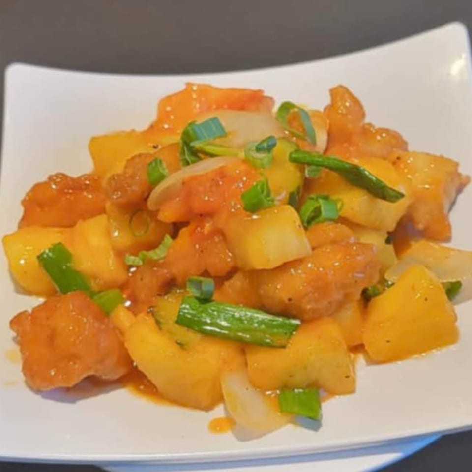 Sweet and sour chicken with pineapple, onions, and green onions on a white plate.