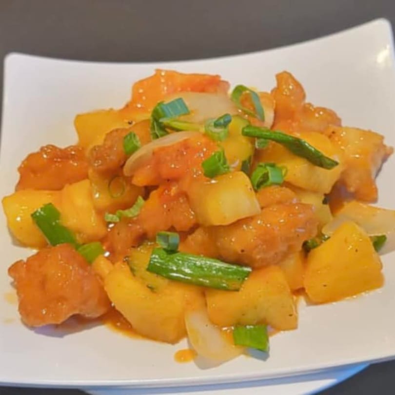 Sweet and sour chicken with pineapple, onions, and green onions on a white plate.
