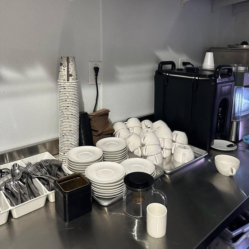 A stainless steel counter with stacks of white cups, saucers, and cutlery for The Corner Restaurant.