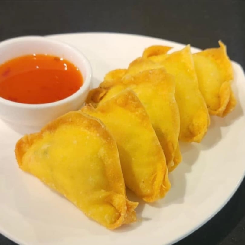 Golden-fried wontons with a side of sweet chili dipping sauce on a white plate.