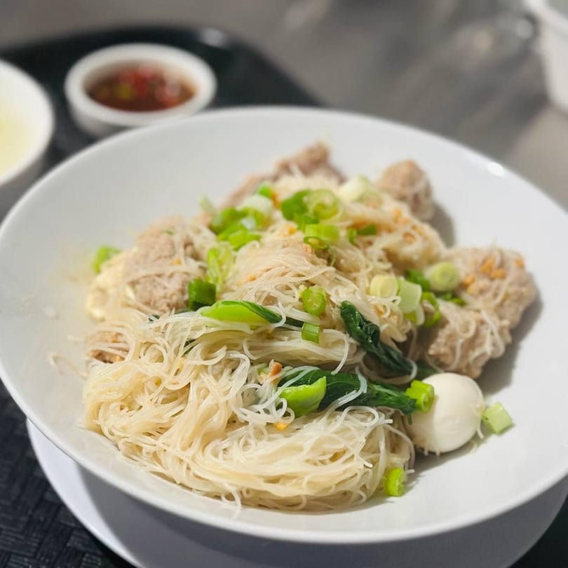 A white bowl of Asian-fusion vermicelli noodles with meatballs, green onions, and bok choy.